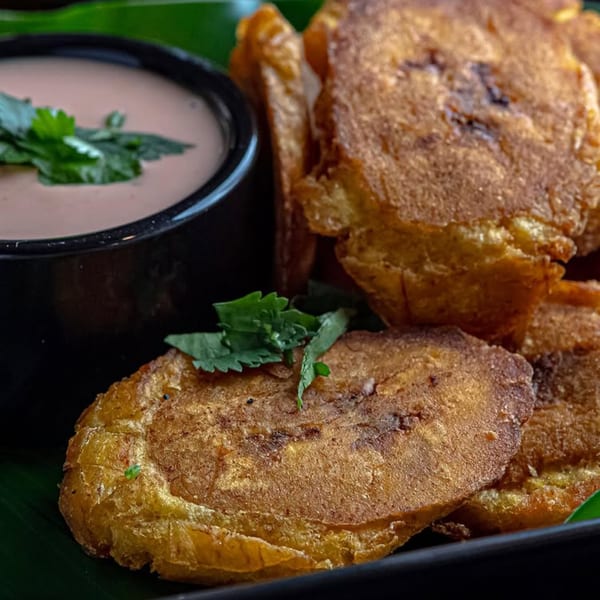 Golden-brown fried plantains with a side of pink dipping sauce garnished with cilantro.