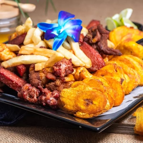 Mamajuana Restaurant's platter of fried plantains, french fries, and various meats, garnished with a blue orchid.