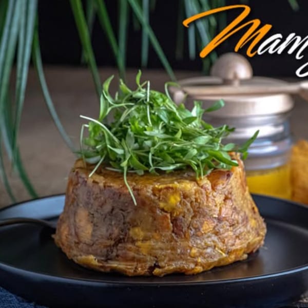 Mofongo topped with fresh greens on a black plate at Mamajuana Restaurant.