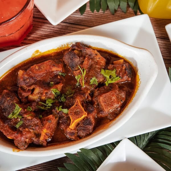 Mamajuana Restaurant's oxtail stew, garnished with fresh herbs, served in a white oval dish.