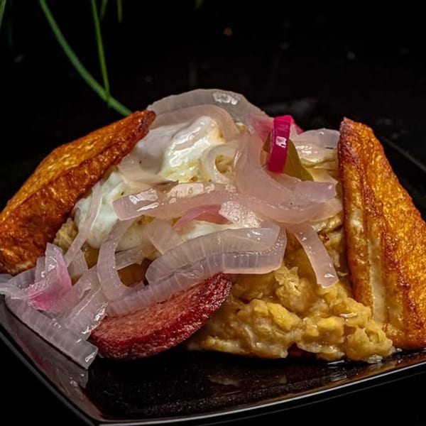 Mofongo with fried cheese, salami, and pickled red onions on a dark plate at Mamajuana Restaurant.
