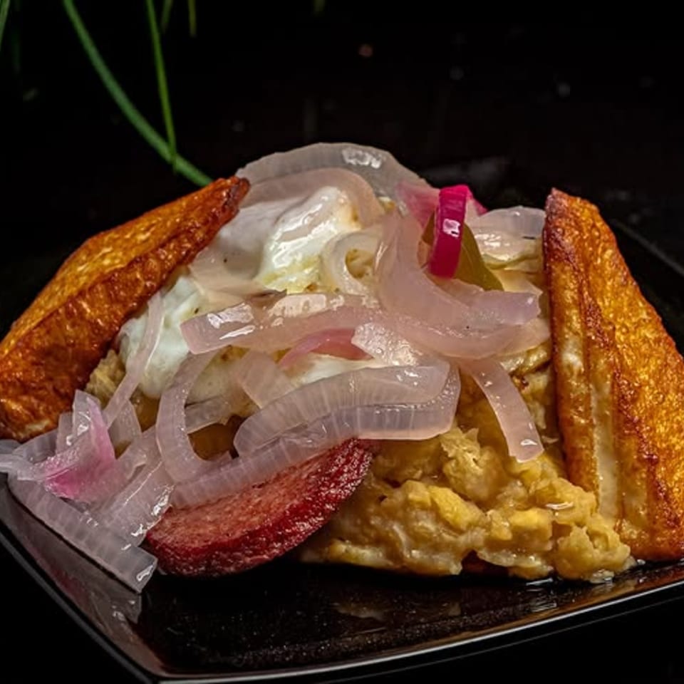 Mofongo with fried cheese, salami, and pickled red onions on a dark plate at Mamajuana Restaurant.