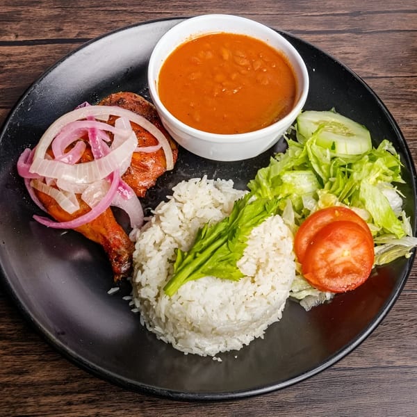 Mamajuana Restaurant's Latin-American dish with chicken, rice, beans, and a fresh salad on a black plate.